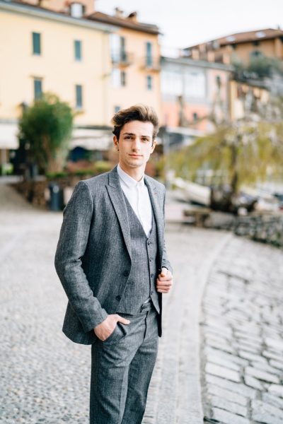 Groom stands on the cobblestones of the street in Varenna against the backdrop of old villas. Lake Como. High quality photo