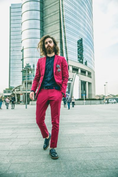 Fashion portrait of a young hipster man walking outdoors with a red formal suit - Unusual businessman going to work